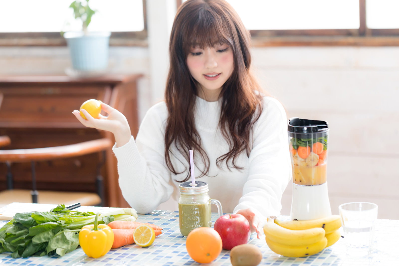 キッチンでスムージー作りの準備をする女性がりんごを手に持っている様子［モデル：河村友歌］