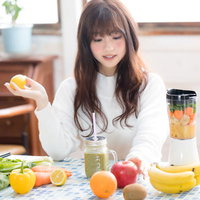 キッチンでスムージー用の果物を手に取る女性の写真