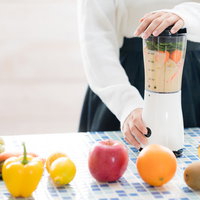 ジューサーで緑色のスムージーを作る手元とカウンターの写真