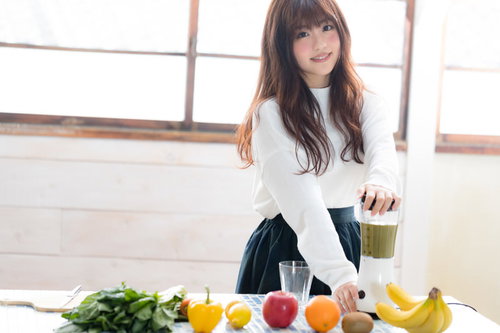 グリーンスムージーを作る若い女性と新鮮な野菜と果物