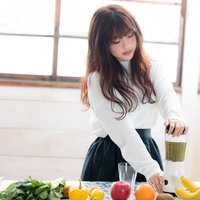 明るいキッチンでジューサーを使ってグリーンスムージーを作る女性の写真