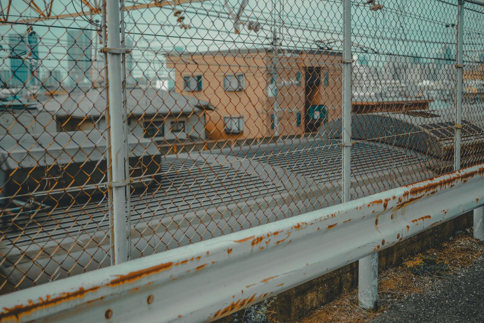錆びたガードレールと金網フェンス越しの工場地帯