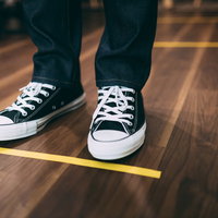 ソーシャルディスタンス中の床に引かれた黄色いライン上に立つ足元の写真