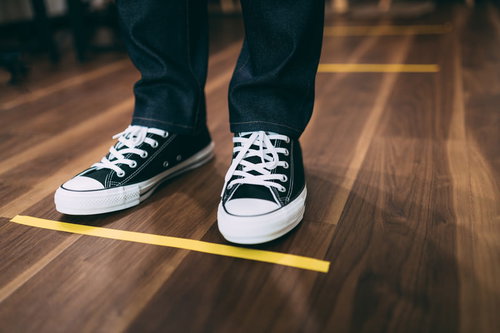 ソーシャルディスタンス中の床に引かれた黄色いライン上に立つ足元