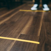 木目の床に黄色いテープで示す間隔をあけてお並びくださいの写真