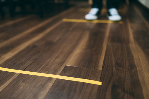 木目の床に黄色いテープで示す間隔をあけてお並びください