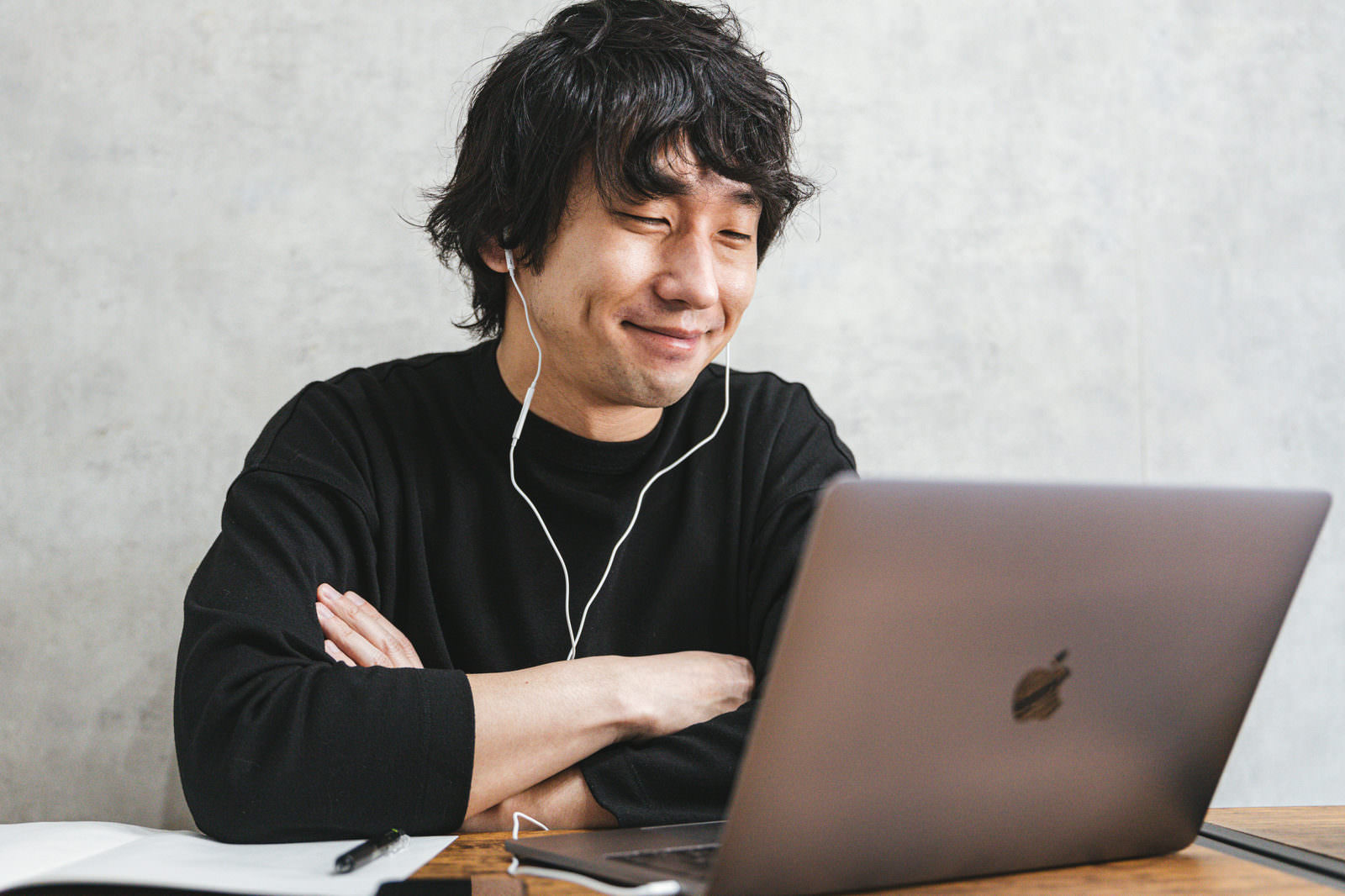 パソコンの前で腕を組み微笑む黒いTシャツの男性［モデル：大川竜弥］