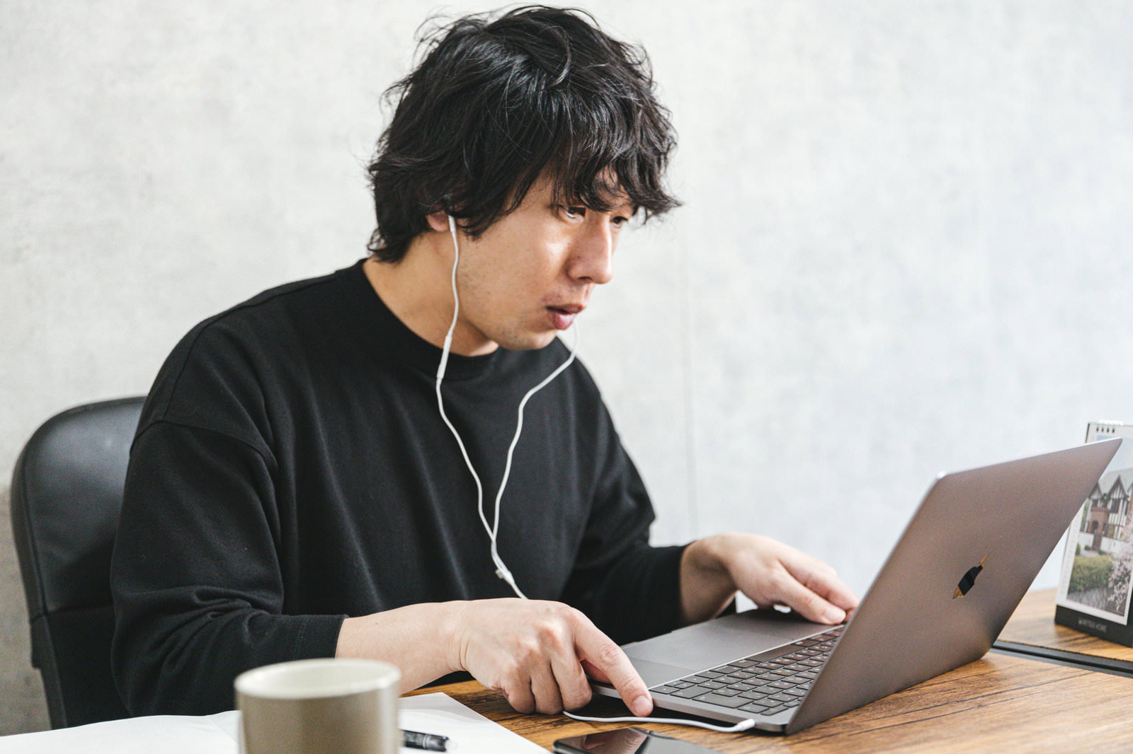 イヤホンをつけて黒いTシャツを着た男性がノートパソコンで作業している様子［モデル：大川竜弥］