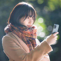 寒い屋外でスマホを見ながら到着を待つ彼女の写真