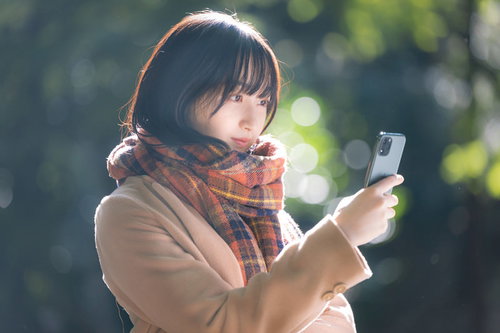 寒い屋外でスマホを見ながら到着を待つ彼女