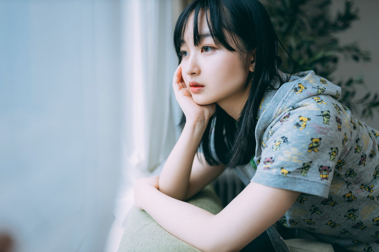 窓際で頬杖をつき憂鬱そうな表情を浮かべる女性［モデル：井隼そら］