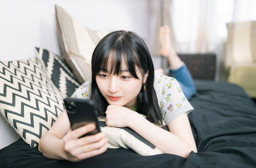休日のスマホは時間泥棒、ベッドで寝転ぶ女性