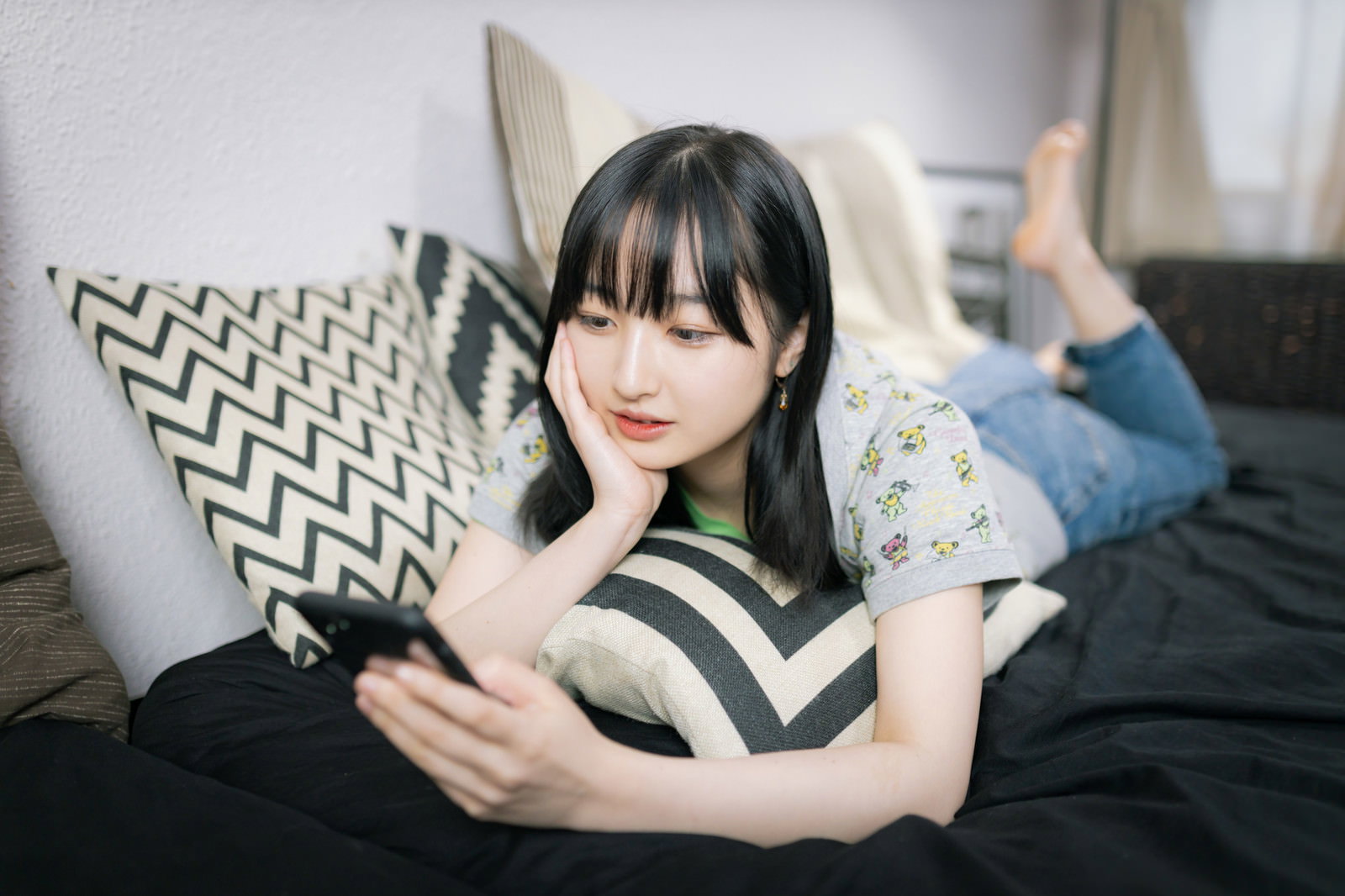 ソファーで寝転んでスマートフォンを見る女性［モデル：井隼そら］