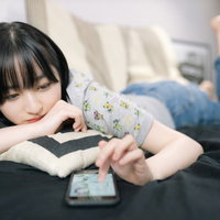 スマホアプリに熱中する休日を過ごす女子大生の写真