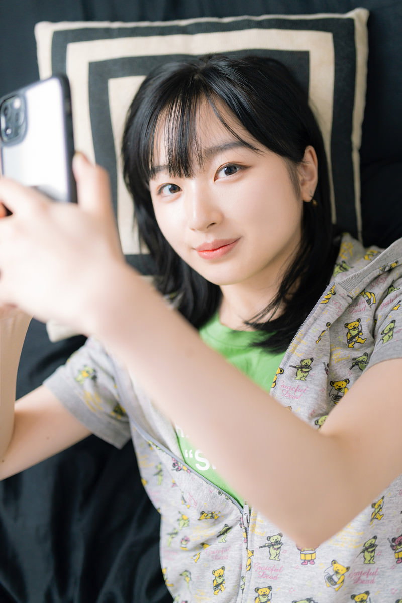 白いシャツを着た女性が横になりながらスマートフォンを操作している［モデル：井隼そら］