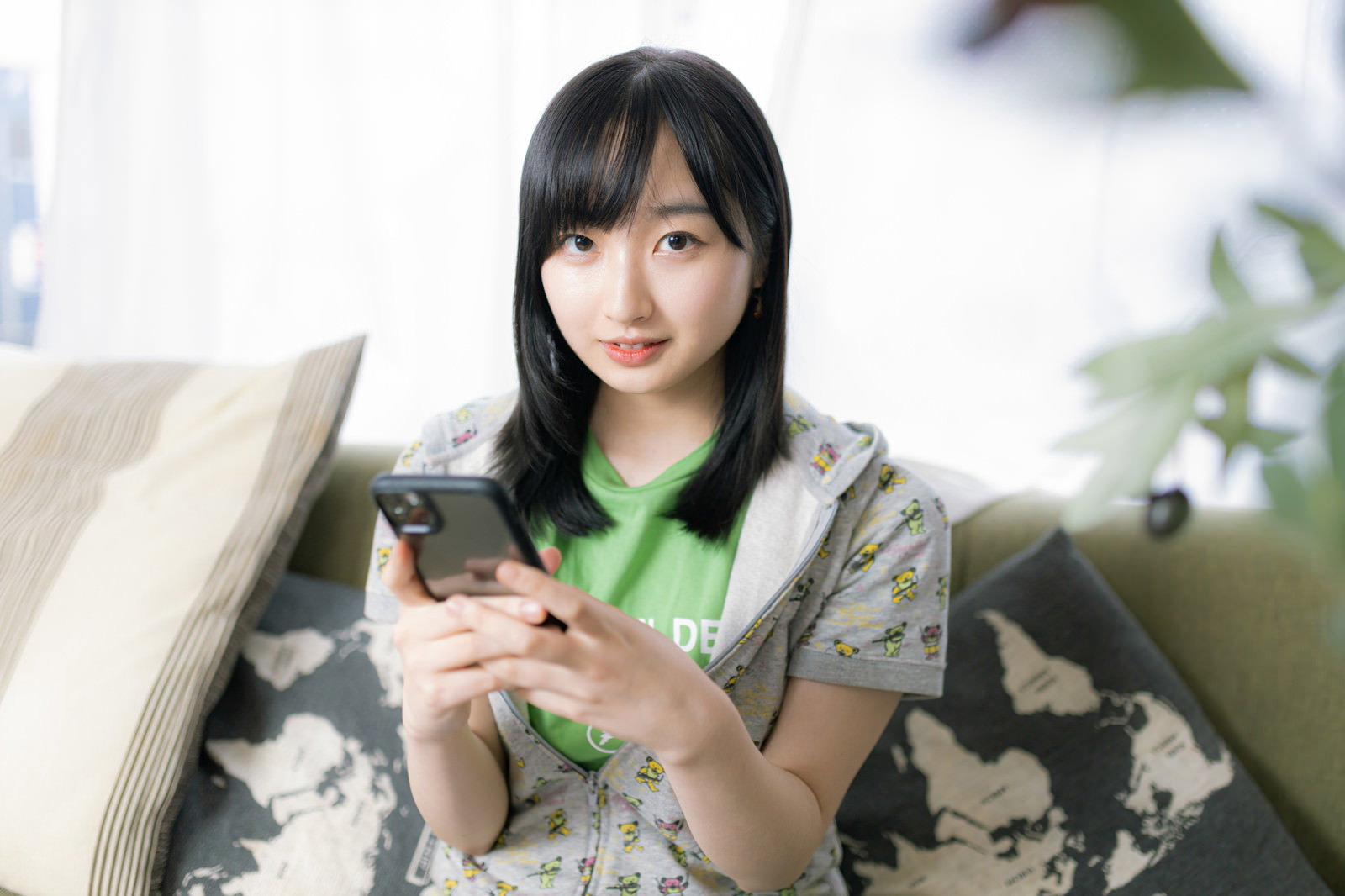 白いソファに座ってスマートフォンを操作する女性［モデル：井隼そら］