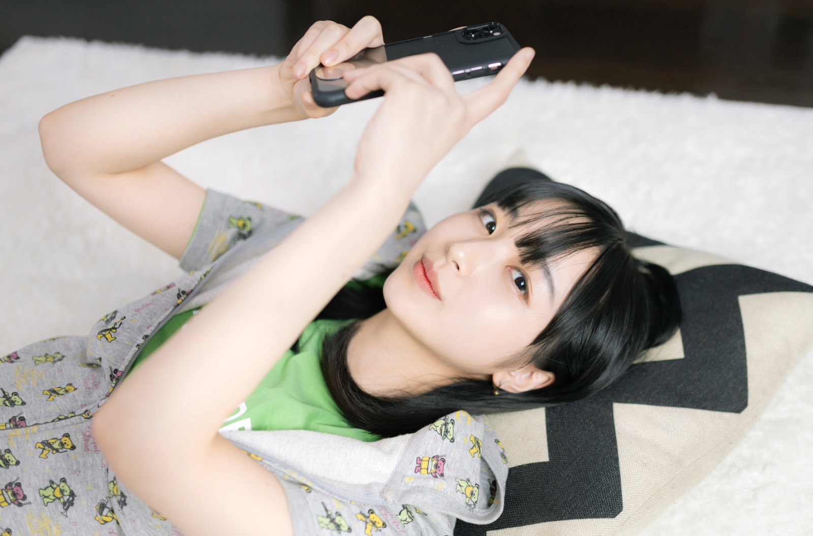 ベッドに横たわりスマートフォンを見る部屋着姿の女性［モデル：井隼そら］