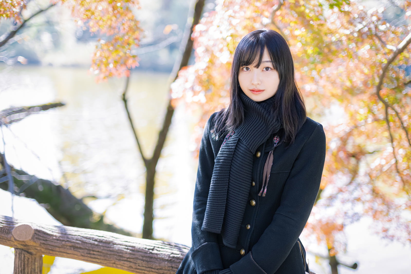 井の頭公園で待ち合わせをする黒いコートを着た女性と秋の紅葉［モデル：井隼そら］