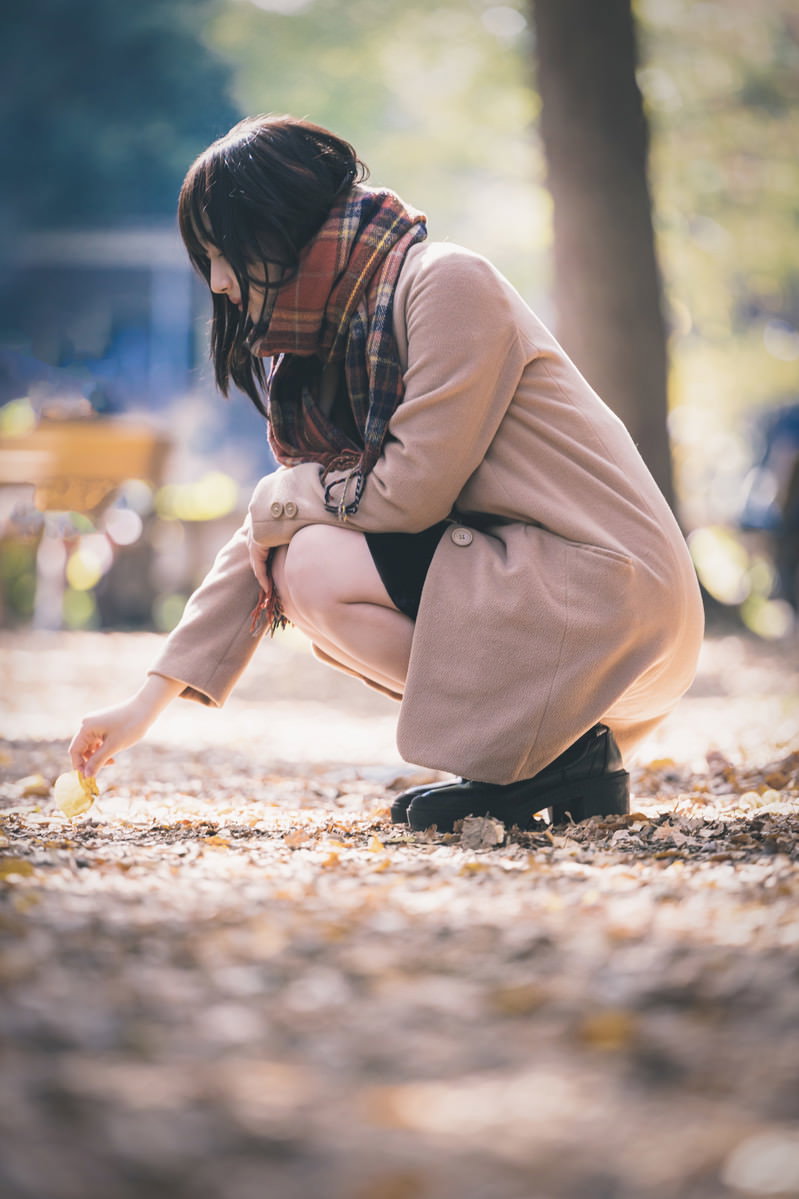 ベージュのコートを着た女性が地面にしゃがんで落ち葉を拾っている［モデル：井隼そら］