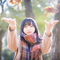茶色のマフラーを巻いて落ち葉を投げ上げる女子の写真