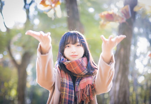 茶色のマフラーを巻いて落ち葉を投げ上げる女子