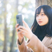 木漏れ日の中でスマホを見る待ち合わせ女子の写真