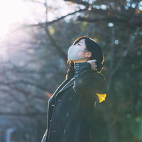 暖かい日向ぼっこで木漏れ日を浴びるマスク着用の女性の写真