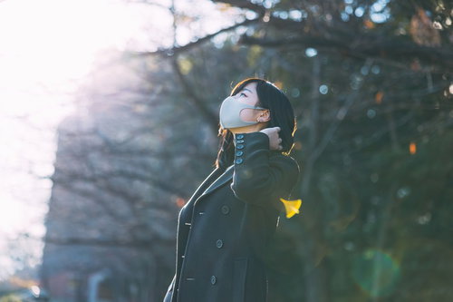 暖かい日向ぼっこで木漏れ日を浴びるマスク着用の女性