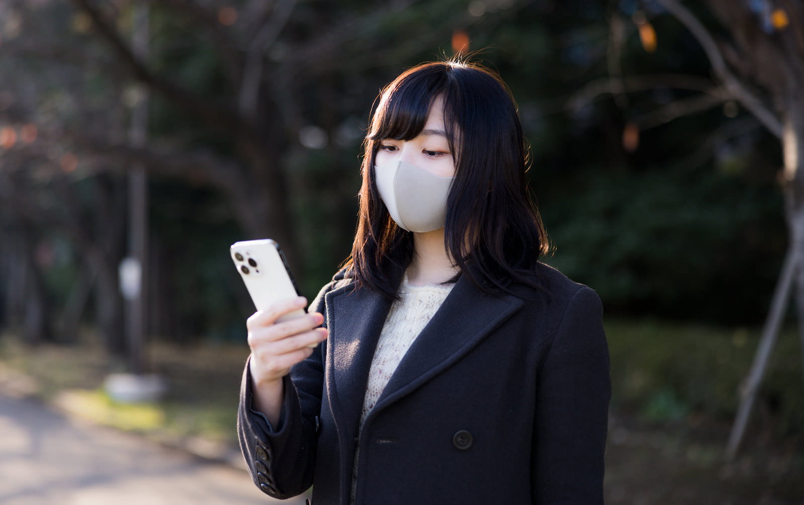 黒いコートを着てマスクをした女性がスマートフォンを見て呆れている［モデル：井隼そら］