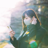 夕暮れ時にスマートフォンで通知をチェックするマスク女子の写真