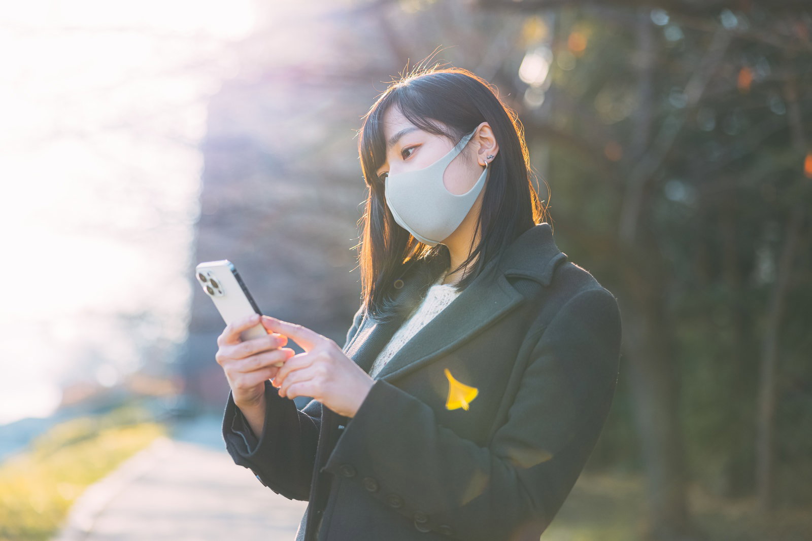 マスクを着用してスマートフォンを見つめる女性［モデル：井隼そら］