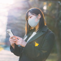 待ちぼうけをくってスマホを眺めるマスク姿の女性の写真