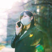 屋外でスマホ通話するマスク姿の女性と緑の自然環境の写真