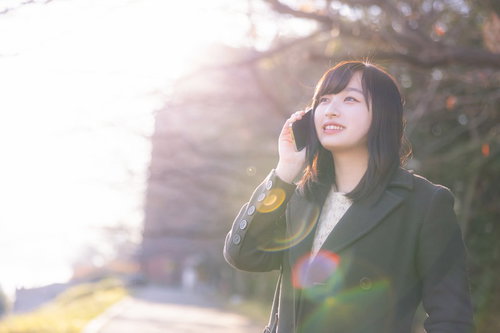 公園で携帯電話をかけて通話する女性、待ち合わせシーン