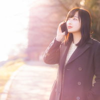 黄昏時に携帯電話で通話するコート姿の女性の写真