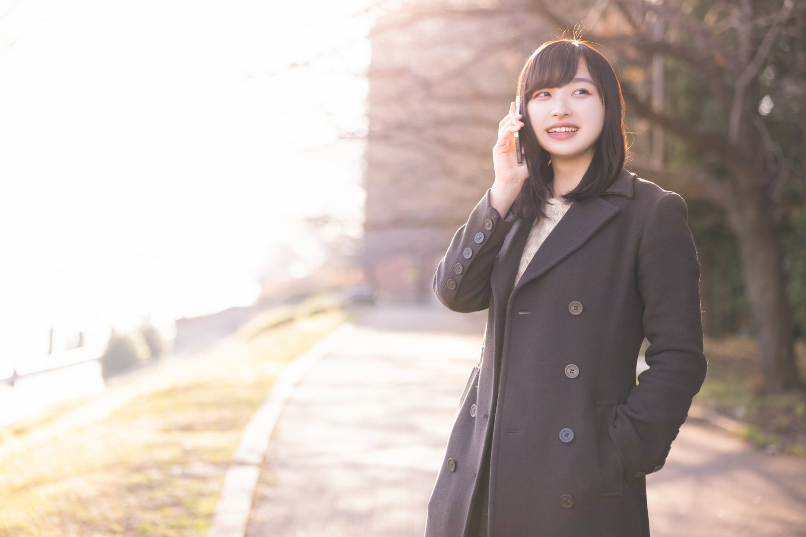 黒いコートを着てポケットに片手を入れ、電話で通話している女性［モデル：井隼そら］