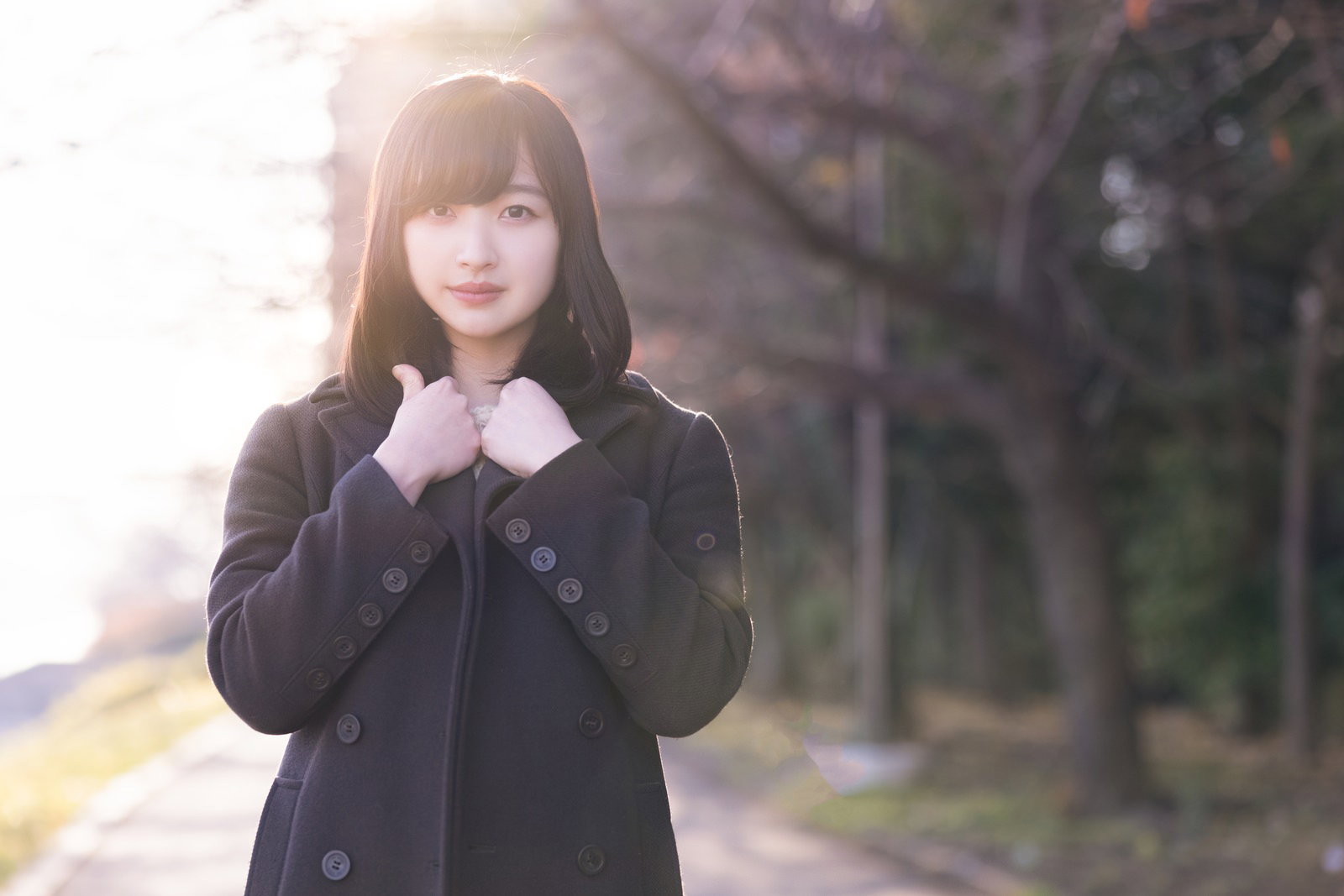 日差しの中で黒いコートを着て立ち止まる女性［モデル：井隼そら］
