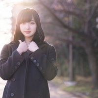 散歩中に立ち止まり日向ぼっこをする黒いコートの女性の写真