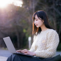 今日の報告書だけ送っちゃうね、白いセーターを着てノートパソコンで作業する女性の写真