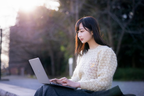 今日の報告書だけ送っちゃうね、白いセーターを着てノートパソコンで作業する女性