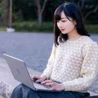 公園のベンチでネットサーフィンする女性の写真