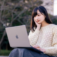 考えながらノートパソコンでメッセージを打つ女性の写真