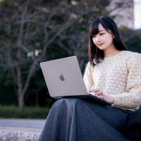 ベンチでノートパソコンを操作してオンライン会議に参加する女性の写真
