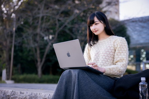 ベンチでノートパソコンを操作してオンライン会議に参加する女性