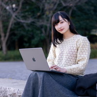 公園のベンチでMacbookを使って作業する女子大生の写真