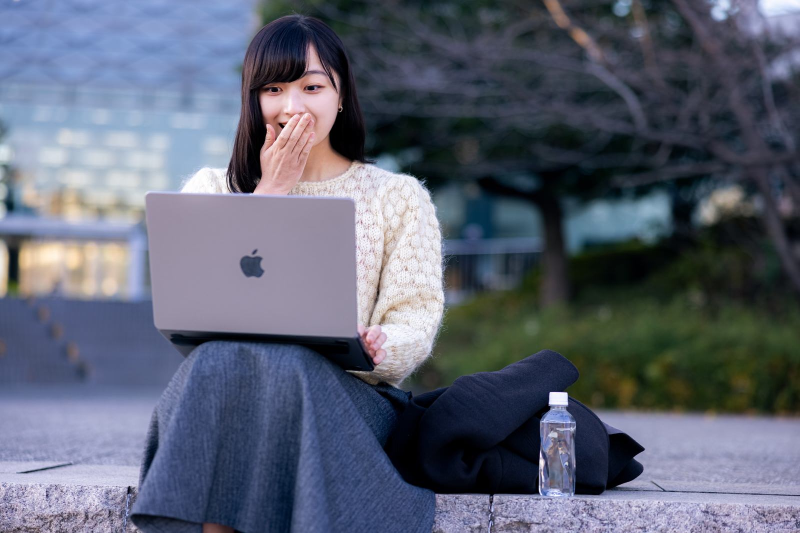 口元に手を添えて驚く表情を見せるリモートワーク中の女性［モデル：井隼そら］
