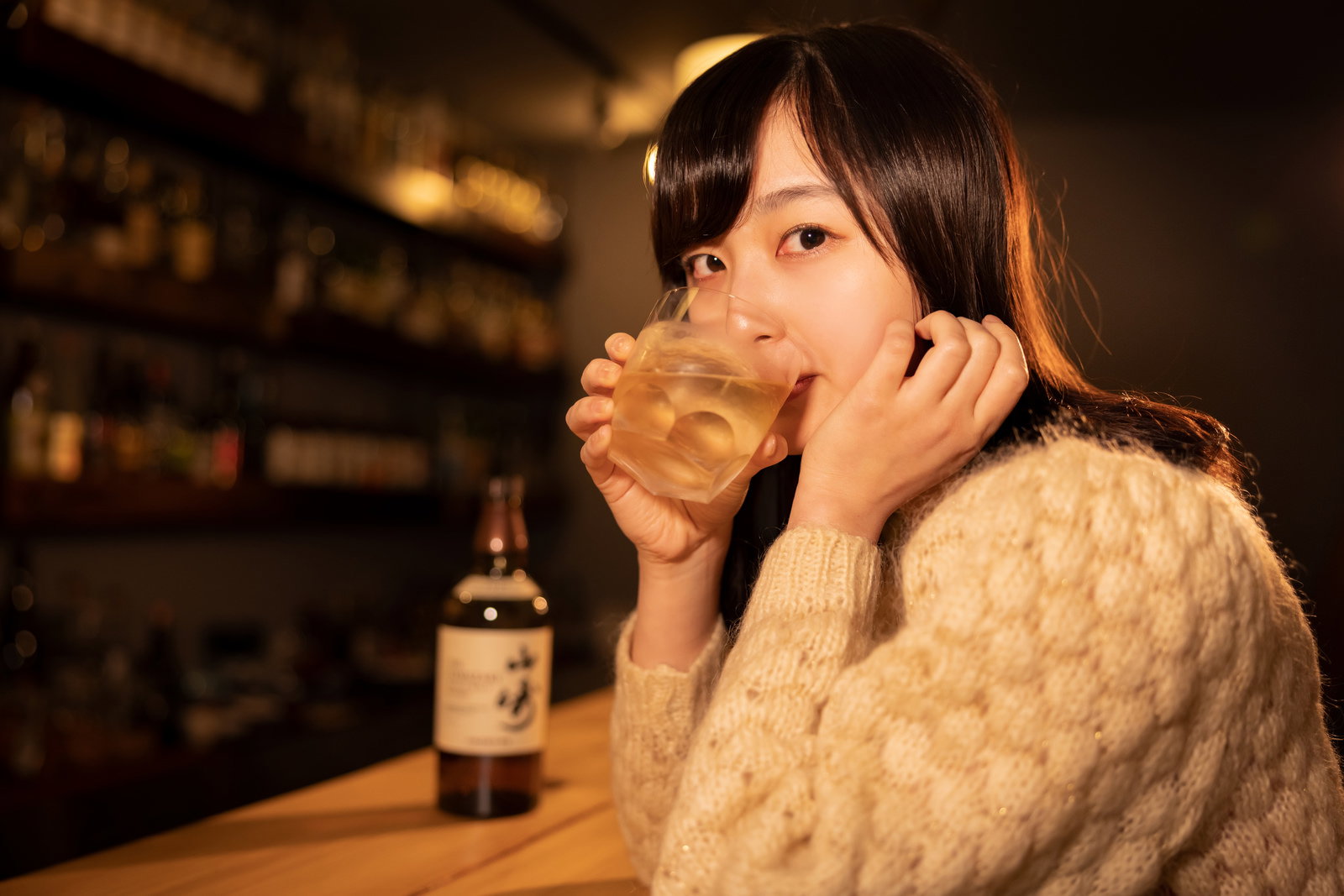 バーのカウンター席でウイスキーグラスを持つ女性［モデル：井隼そら］