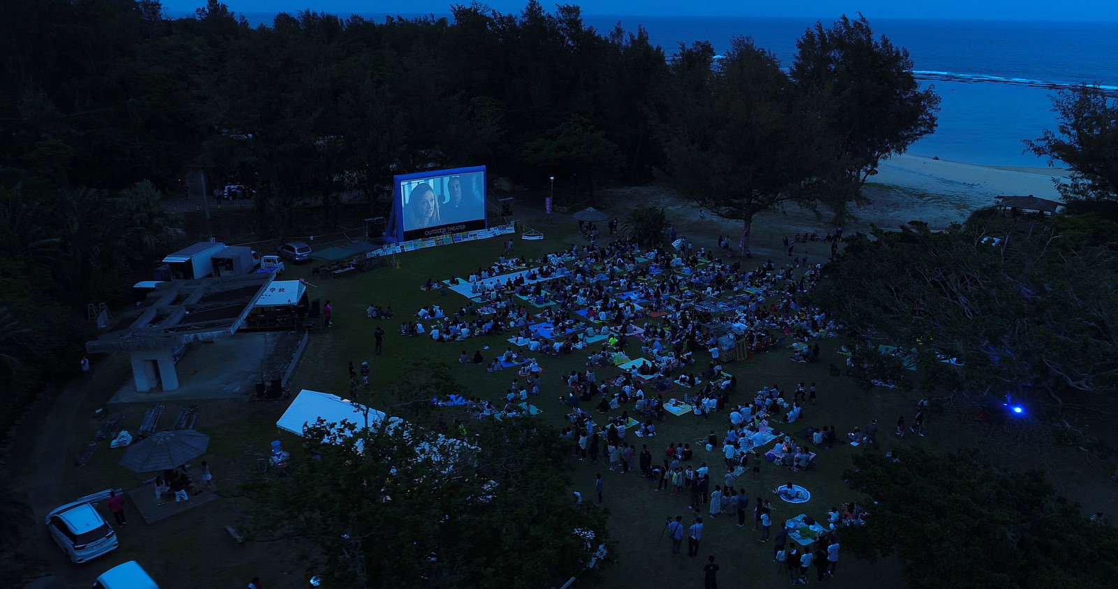 夜空の下、大型スクリーンの前に集まった観客たちが野外映画を楽しむアウトドアシアターの様子