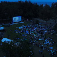 夜間のアウトドアシアターで映画を楽しむ観客たちの写真