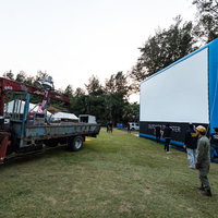 青空の芝生でアウトドアシアターの大型スクリーンを設営中の写真